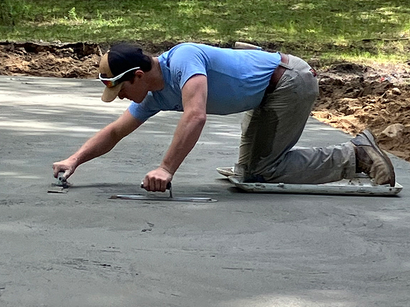 Trapanier-Masonry-Team-4 An employee is leveling a driveway with metal trowels.