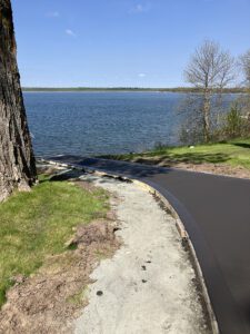A view of a lake with a concrete sidewalk gong to do it.