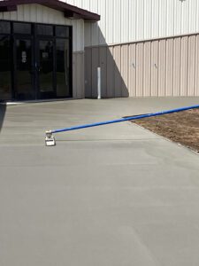 A concrete worker is smoothing out a cement sidewalk outside of a business.