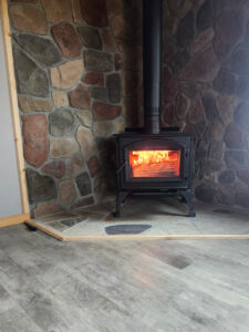 Custom natural stone fireplace with a black wood-burning stove installed on a stone hearth in a residential home.